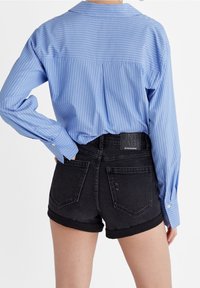 Chemise rayée bleue à manches longues et col ; associée à un short en denim noir avec ourlets roulés et deux poches arrière.