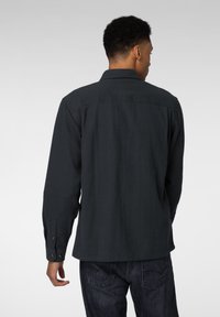 Svart skjorte med knapper og lange ermer, med rett snitt og bakparti, kombinert med mørke denimjeans.