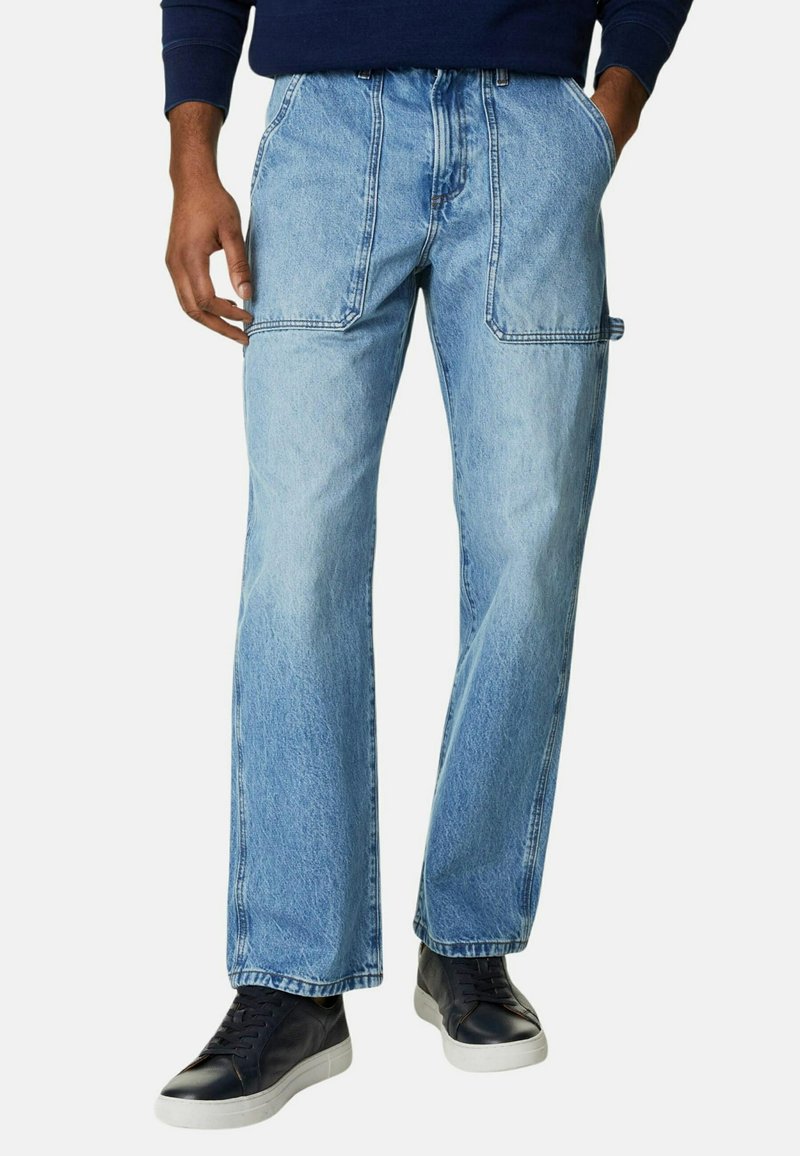 Jeans de mezclilla azul claro con un corte relajado, que cuentan con dos bolsillos frontales y dos bolsillos laterales tipo cargo, combinados con zapatillas oscuras.