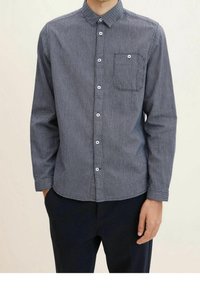 Camicia button-up di colore blu navy con un piccolo motivo testurizzato. Presenta una singola tasca sul petto e bottoni bianchi sul davanti e sui polsini.