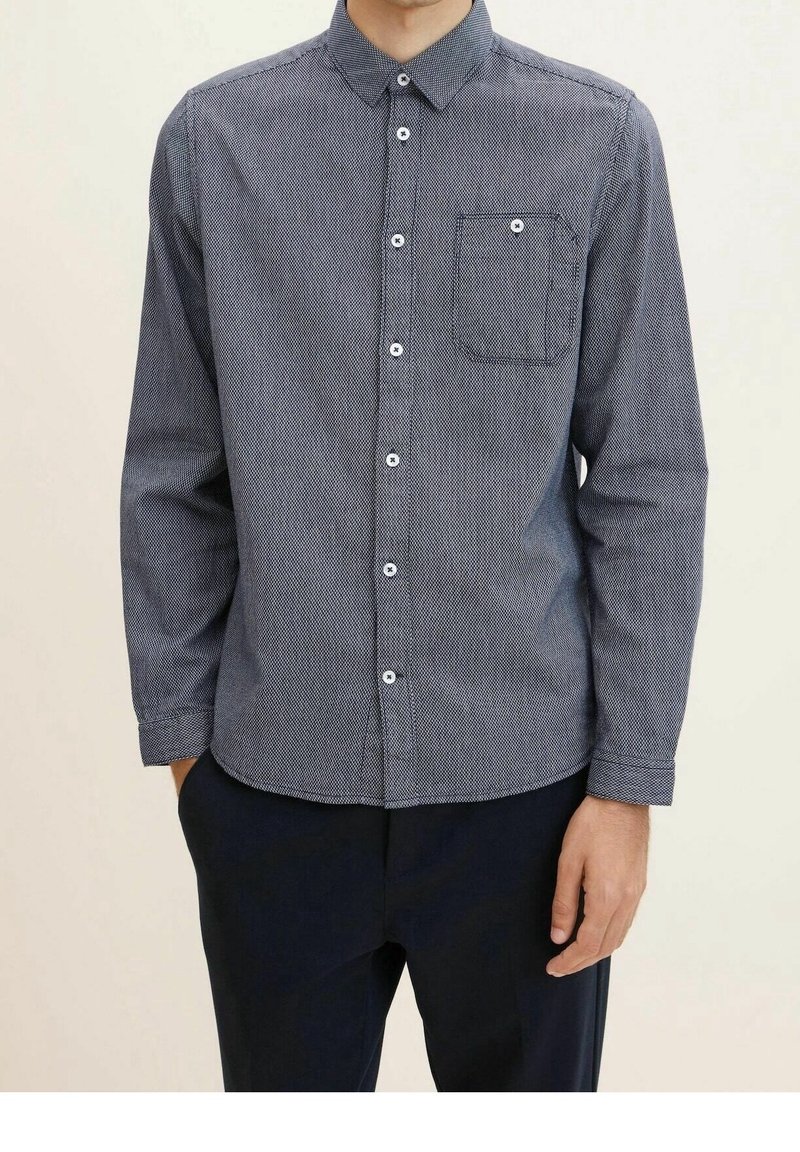 Camicia button-up di colore blu navy con un piccolo motivo testurizzato. Presenta una singola tasca sul petto e bottoni bianchi sul davanti e sui polsini.