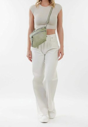 Groene leren crossbodytas met twee ritsvakken, verstelbare band en een gladde textuur. Draagt wit wijde broekspijpen en een beige top.