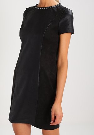 Czarna sukienka z krótkim rękawem o subtelnej fakturze i detalach z przeszywanych paneli, z okrągłym dekoltem ozdobionym małymi metalowymi kółkami.