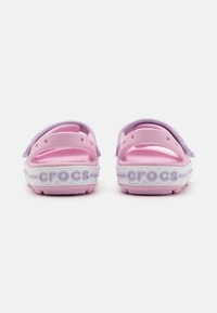 Roosa ja lilla Crocs, millel on tekstuuriga pind, taga rihmad ja valged tallad. Omaduseks on üles tõstetud "crocs" bränding kandadel.