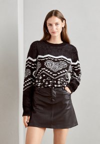 Pullover nero peloso con un motivo geometrico bianco, abbinato a una mini gonna in pelle nera. Il top ha maniche lunghe e scollo rotondo.