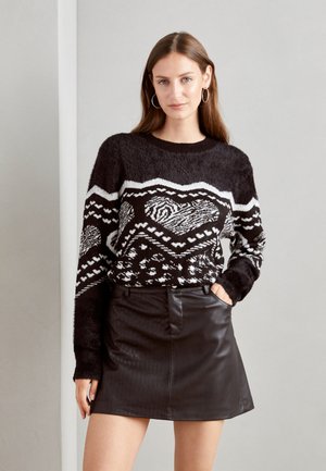 Pullover nero peloso con un motivo geometrico bianco, abbinato a una mini gonna in pelle nera. Il top ha maniche lunghe e scollo rotondo.