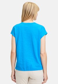 Niebieska bluzka z krótkim rękawem, ozdobiona teksturowanym wzorem, okrągłym dekoltem i luźnym krojem. Materiał gładki z delikatnym połyskiem.