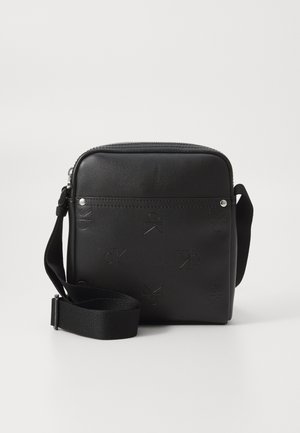 Bolso cruzado de cuero negro con cierre de cremallera, patrón de logo en relieve, correa plana y herrajes en tono plateado. Acabado liso con una forma estructurada.