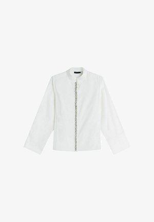 Biała koszula z długim rękawem, zapinana na guziki, z kołnierzykiem i dekoracyjnym srebrnym łańcuszkiem biegnącym pionowo wzdłuż przodu.