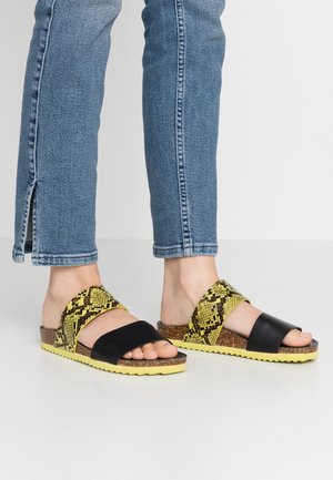 Sorte og gule mønstrede sandaler med korksål og teksturerede stropper, der har en zigzagkant og et åbent tådesign.