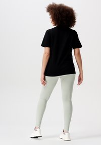 Zwarte t-shirt met korte mouwen en een ontspannen pasvorm, gecombineerd met lichtgroene ribbelleggings en witte sport schoenen.