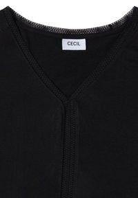 Col en V noir de chemise avec une fine bordure en dentelle et une étiquette blanche portant la mention "CECIL" cousue à l'intérieur du col.