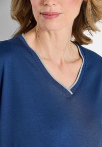 Marineblaues V-Ausschnitt-Oberteil aus glattem Stoff, mit silbernem Besatz entlang des Ausschnitts und einem lässigen Schnitt für maximalen Komfort.