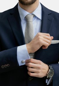 Veste de costume marine avec chemise bleu clair et cravate gris clair à motif en losange. Manchettes en argent et montre accentuent le look.