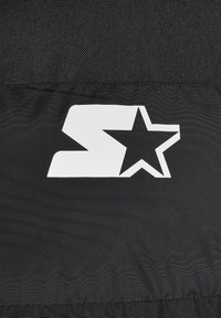 Juodas audinys su ryškiu baltu logotipu, kuriame pavaizduota "S" ir žvaigždė, pasižymi lygiu paviršiumi ir kontrastinga spalvų kompozicija.