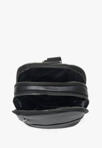 Černá kožená taška se dvěma zipovými přihrádky. Vyznačuje se texturovaným povrchem a jednoduchým designem, který ukazuje funkční vnitřní prostor.