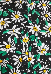 Tissu noir avec des marguerites blanches, des centres jaunes et des feuilles vertes, comportant un devant boutonné et deux poches poitrine.