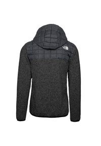 Grå isolerad jacka med quiltad huva och övre panel, med texturerat nedre tyg. Logotypen är placerad på övre högra sidan.