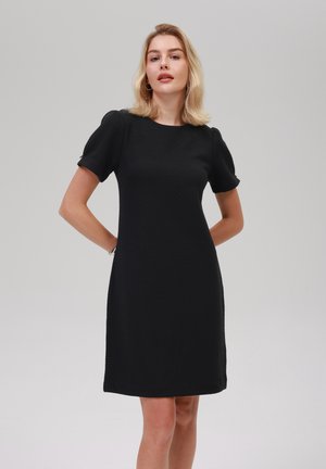 Robe en coton noire avec un tissu texturé, manches bouffantes courtes et un col rond classique. Elle arrive juste au-dessus du genou.
