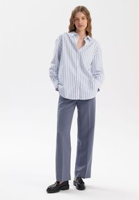 Koszula w paski w kolorze niebiesko-białym, połączona z prostymi szarymi spodniami i czarnymi mokasynami; luźny krój z kołnierzykiem i długimi rękawami.