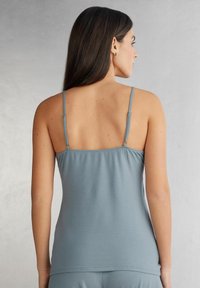 Jasnoniebieski top na ramiączkach o cienkich spaghetti. Gładki, elastyczny materiał z dopasowanym krojem, z prostym dołem i podstawowym tyłem.