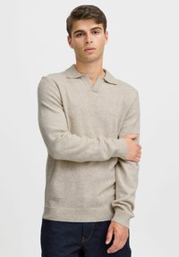 Beige pulóver, V-nyakkivágással és gallérral. Puha tapintás, bordás mandzsetta és alj, sötétkék farmernadrággal párosítva.