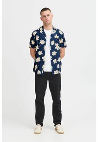 Camicetta a maniche corte blu navy con motivo floreale bianco e rosso, abbinata a pantaloni neri e sneakers bianche con strisce beige.
