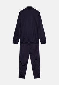 Tuta di colore blu navy realizzata in un tessuto morbido e leggero, con colletto zip, polsini elastici e una vita elastica sui pantaloni.