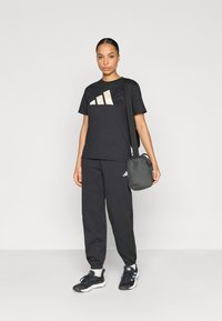 Μαύρο μπλουζάκι Adidas με μπεζ λογότυπο, μαύρη φόρμα και μαύρα αθλητικά παπούτσια. Η εμφάνιση συμπληρώνεται με μια μικρή μαύρη τσάντα με ιμάντα ώμου.