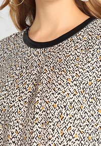 Mönstrad tygtröja med svart rund halsringning. Designen innehåller svarta, vita och senapsgula abstrakta former.