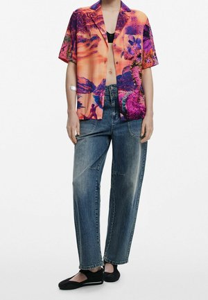 Persoon draagt een levendig oranje en paarse tropische print korte mouw shirt, losse blauwe spijkerbroek, zwarte bh en zwarte instapschoenen.