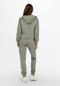 Ljusgrön sweatshirt med huva och matchande joggers, med elastiska muddar och midjeband. Texturerad tyg med en slät yta.