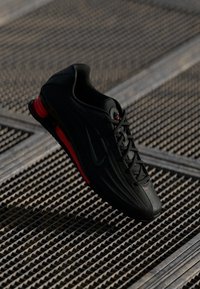 Crne i crvene Nike tenisice za trčanje s vidljivom zračnom jastučićem na metalnoj rešetkatoj površini.