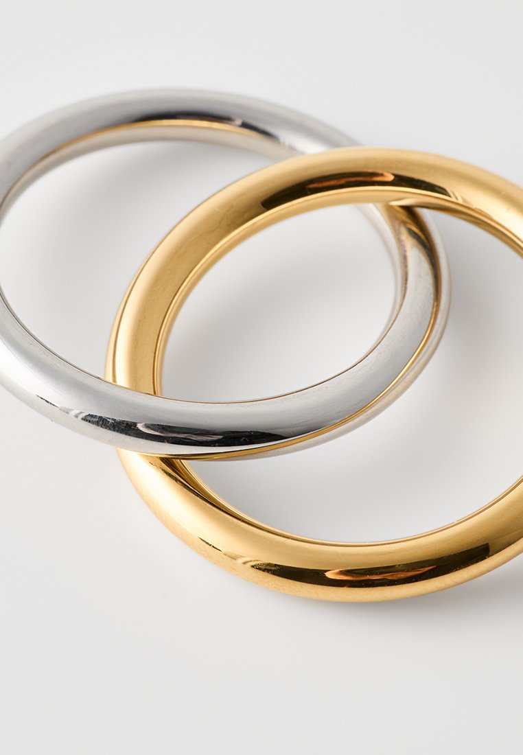 Trois anneaux lisses empilés ensemble : un argent, un or et un autre or. Les anneaux ont une finition polie et un design arrondi.