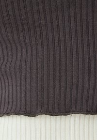 Gebreid sweater met een donkergrijze ribstructuur aan de bovenkant, die overgaat in crèmekleurige ribstof aan de onderkant met een rauwe zoom.