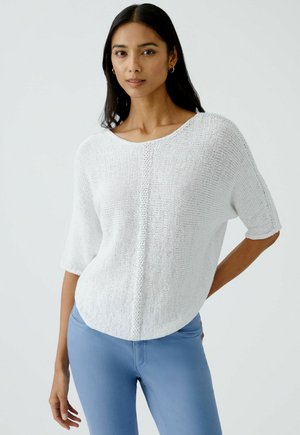 Weißer, gestrickter Pullover mit kurzen Ärmeln und Rundhalsausschnitt, mit lockerem Schnitt und strukturiertem Muster. Kombiniert mit hellblauen, engen Jeans.