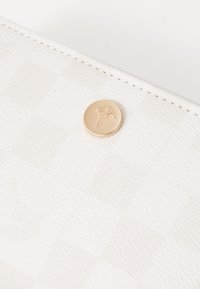 Carteira de pele branca texturizada com um discreto padrão riscado e um botão circular em tom dourado com um design floral em relevo.