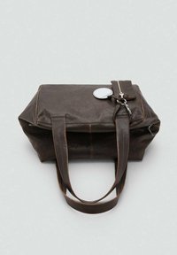 Bruine leren totebag met dubbele handvatten, een klein ritssluitingsetui eraan vast, en een ronde metallic tag op een lichte achtergrond.