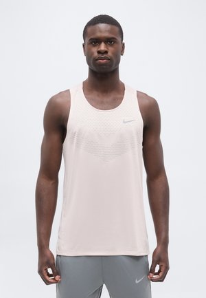 Homme athlétique portant un débardeur Nike rose clair sans manches et un short gris, debout sur un fond clair uni.