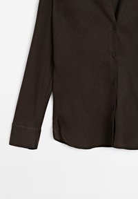 Chemise marron foncé à manches longues avec boutons, ourlet arrondi et une seule manchette visible sur un fond clair uni.