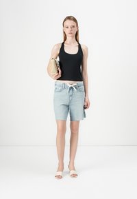 Black sleeveless top, light blue denim shorts, and beige slide sandals. Carrying a small, textured gold handbag. Simple, casual outfit.