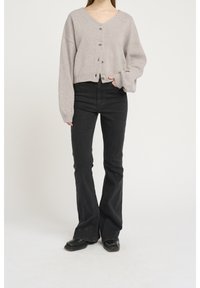 Grå stickad kappa med djup V-ringning, oversized passform och fem knappar, tillsammans med utsvängda svarta jeans och svarta skor.