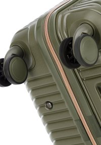 Valise rigide de couleur vert olive avec une texture rayée verticale, fermeture éclair en cuivre et deux roues noires pour la mobilité.