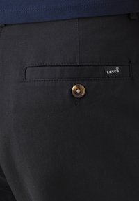 Pantalon noir à la texture lisse, avec une poche arrière dotée d'un rabat rectangulaire, d'un bouton en bronze et d'une étiquette logo Levi's blanche.
