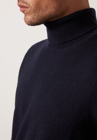 Mörk marinblå polotröja i mjukt, texturerat material. Åtsittande design med hög krage och subtil ribbning vid kragen, som betonar värme och komfort.