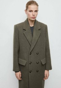 Abrigo de lana mezcla en verde oliva, de doble botonadura, con grandes botones negros, solapas con muesca y bolsillos laterales, que presenta un ajuste sobredimensionado y a medida.