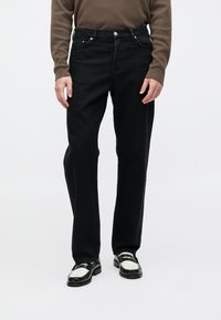 Vaqueros de mezclilla negra con un diseño de pierna recta, cinco bolsillos, cierre de botón y sutiles detalles de costura. Llevados con mocasines en blanco y negro.