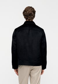 Giacca in camoscio nero con colletto, tasche laterali e taglio dritto. Presenta un design minimalista e una texture liscia.