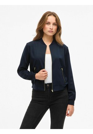Giacca bomber navy con collo alto, chiusura a zip dorata e tasche laterali con zipper. Il tessuto ha una texture liscia e una silhouette aderente.