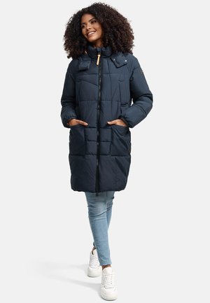 Navy blue puffy coat featuring a high collar, front zipper, two large pockets, and elastic cuffs, paired with light blue jeans and white sneakers.